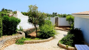 Un patio con senderos de piedra, una pared blanca y arbustos verdes.