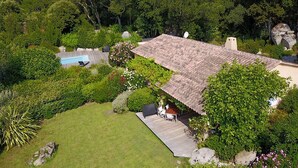 Una casa con una amplia terraza, piscina y abundante vegetación.