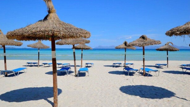 Una spiaggia con ombrelloni di paglia e poltrona a sdraio blu.