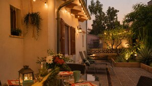 Un'area pranzo all'aperto con tavoli per due, sedie e una varietà di piante e fiori.