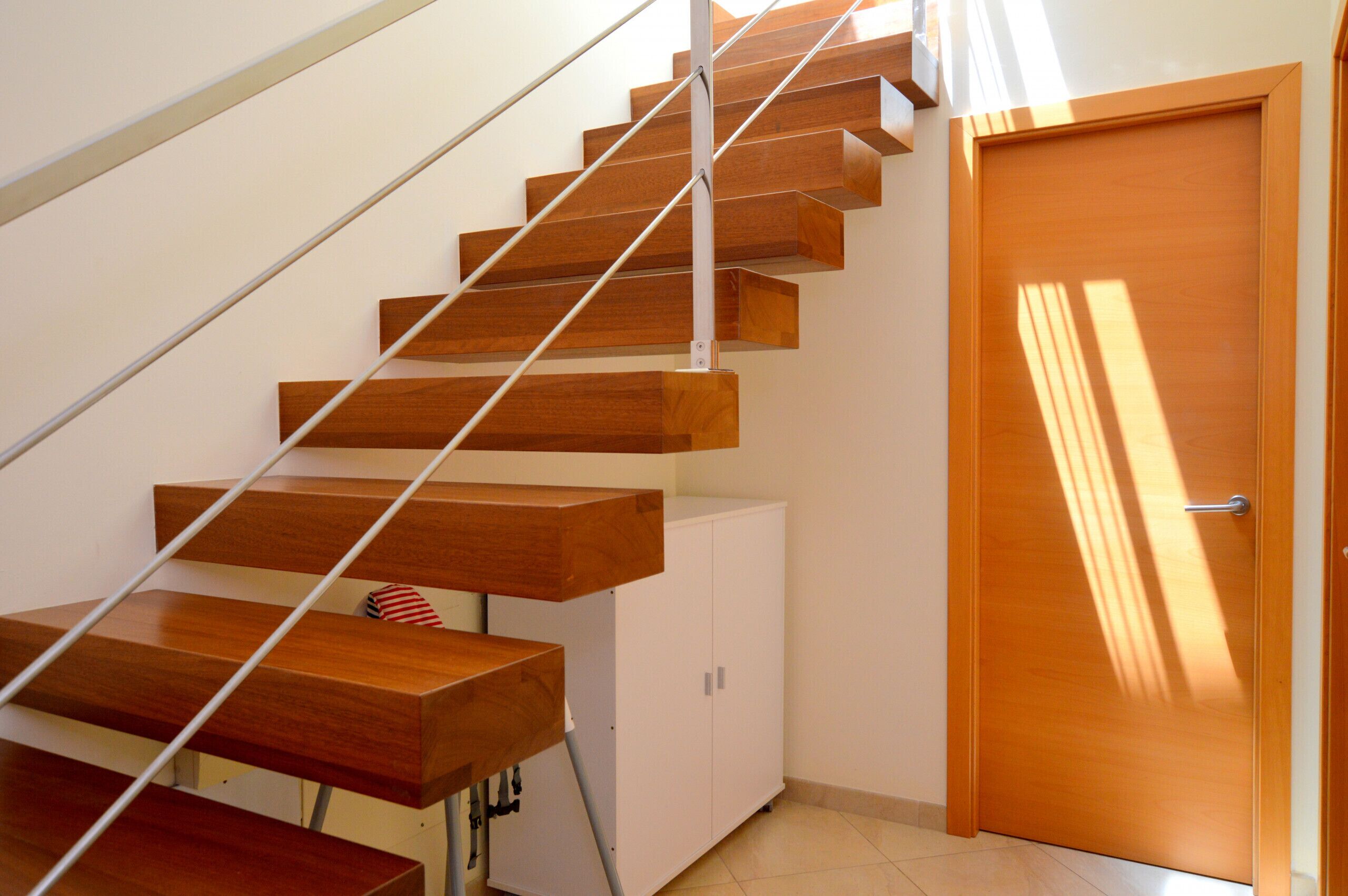 Una escalera de madera con barandilla de metal que lleva a una puerta blanca.