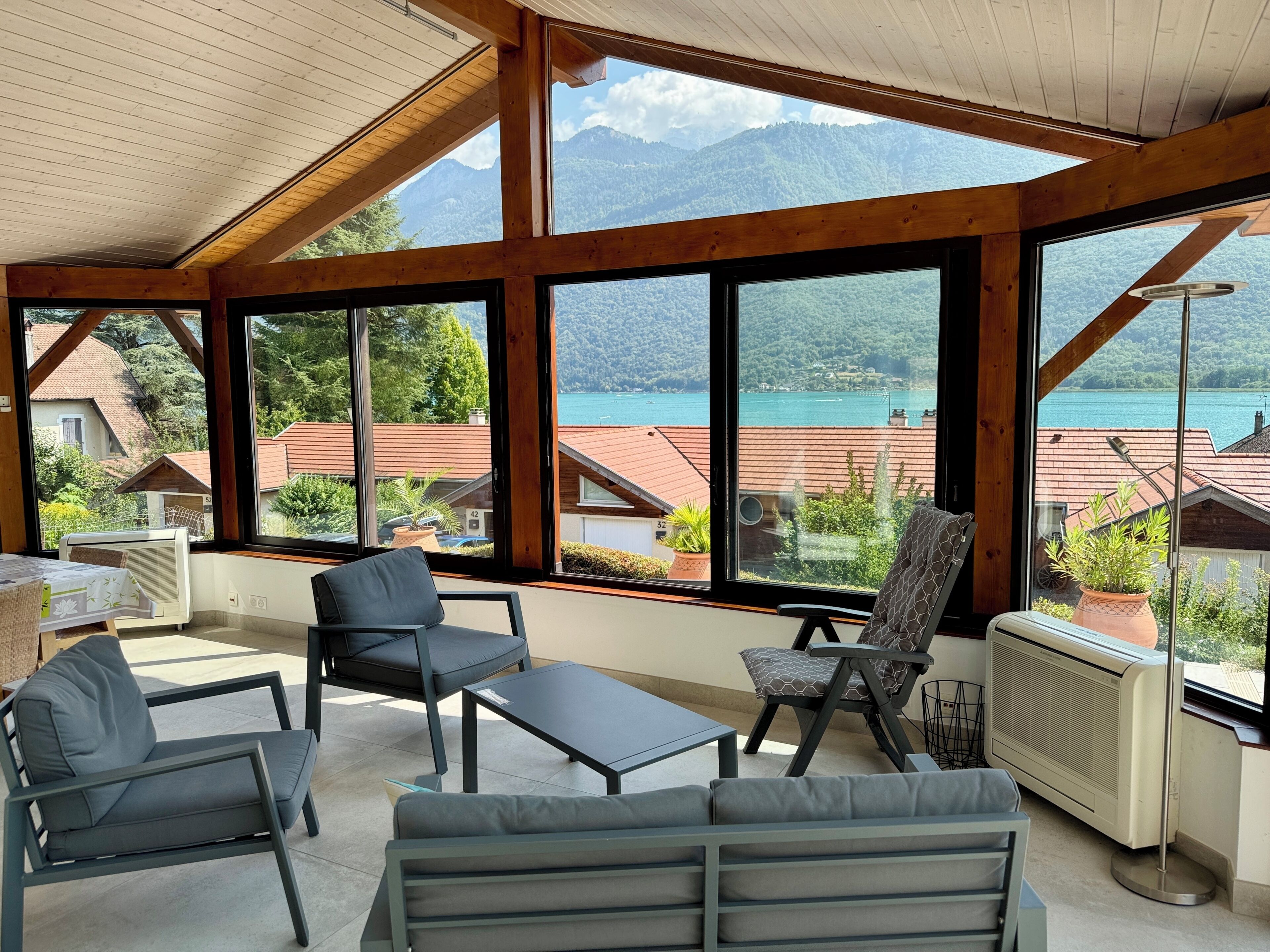 Une pièce baignée de lumière naturelle, avec de grandes fenêtres, un plafond en bois et une vue sur un lac et des montagnes.