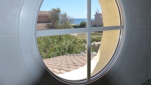 Una ventana circular con vistas a una playa, edificios y vegetación.