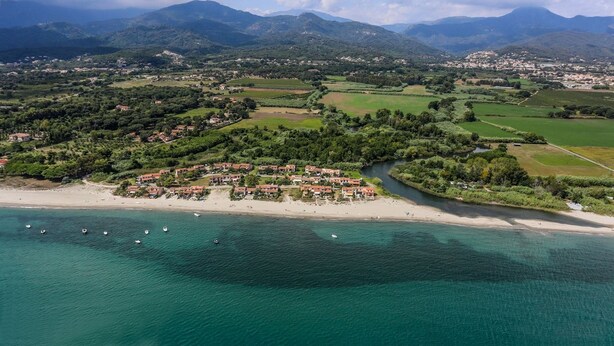 Vista aérea de una zona costera con playa, un conjunto de edificios y vegetación circundante.