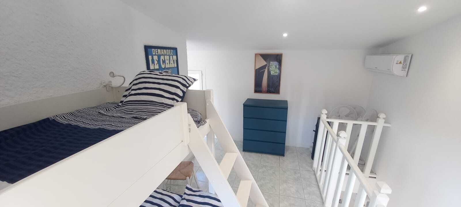 Een compacte slaapkamer met een stapelbed, een klein dressoir, een ingelijst foto aan de muur en een witte balustrade.