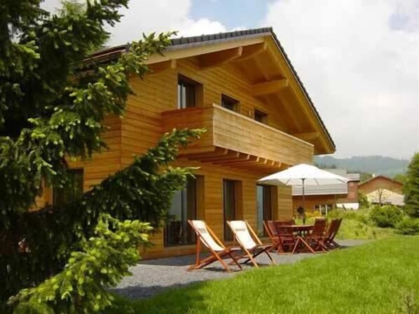 A two-story wooden house with a balcony, a patio with outdoor furniture, and a view of the surrounding landscape. - Stunning detached chalet with a large garden and views, Swiss Alps for 11 people (Leysin)
