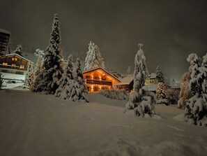 A snow-covered lodge with a wooden exterior and a lit interior, surrounded by snow-laden trees. - Stunning detached chalet with a large garden and views, Swiss Alps for 11 people (Leysin)
