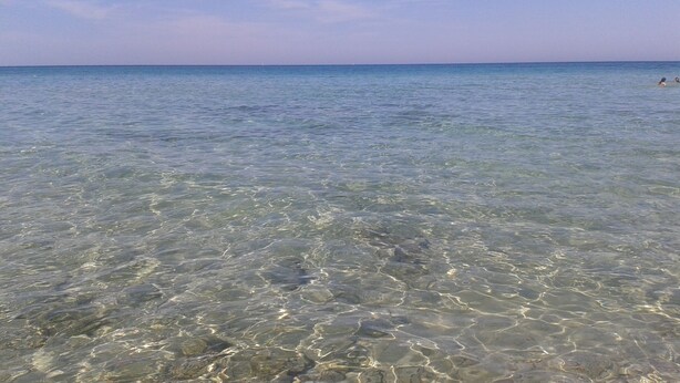 Klarer Blick auf das Meer mit sichtbaren Felsen unter der Wasseroberfläche und einem entfernten Boot.