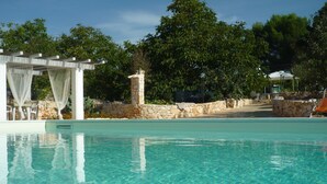 Ein klares Schwimmbecken mit einer Steinmauer und einer Pergola mit weißen Vorhängen.