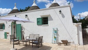 Ein weißes Gebäude mit einer gefliesten Terrasse, einem Tisch mit Stühlen, einer Schubkarre und einer blauen Leiter.