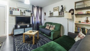 Ein Wohnzimmer mit einem grünen Sofa, einem Flachbildfernseher, einem Couchtisch und einem Bücherregal.