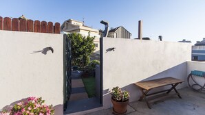 Eine Dachterrasse mit einer Holzbank, Blumentöpfen und Blick auf einen Garten.