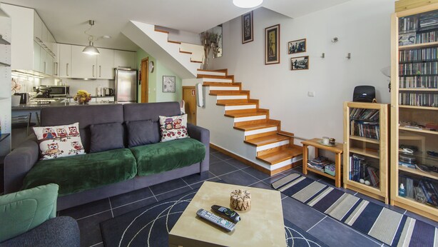 Ein modernes Wohnzimmer mit einem grauen Sofa, einem Couchtisch und einer Treppe, die in eine obere Etage führt.