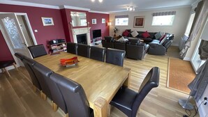 A spacious dining area with a wooden table and black chairs, a fireplace, and a sofa with cushions in the background.
