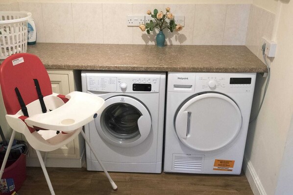 A laundry area with two washing machines, a red child safety seat, and a vase with flowers on the countertop.