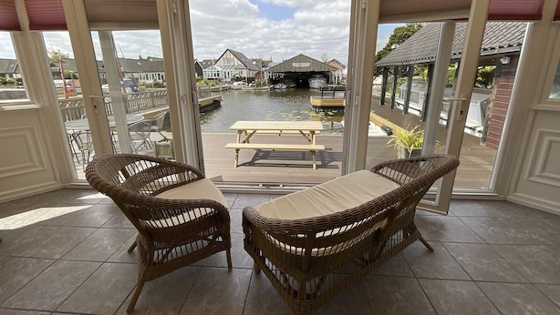 A covered patio with wicker furniture and a view of a canal and buildings.