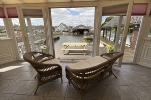 A covered patio with wicker furniture and a view of a canal and buildings.