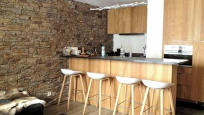 Una cocina moderna con pared de piedra, taburetes de bar de madera y horno empotrado.
