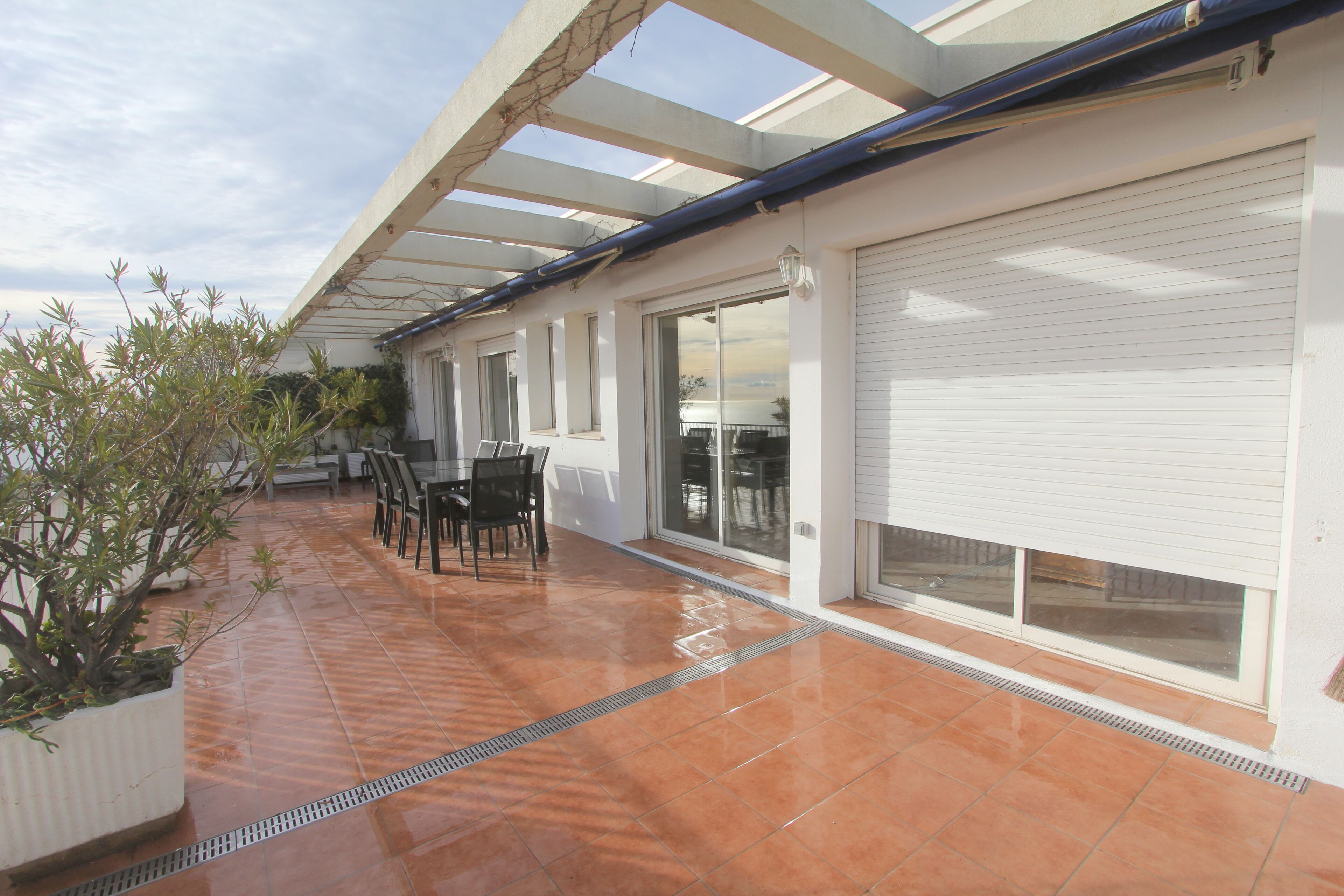 A covered patio with a tiled floor, outdoor furniture, and a white garage door.