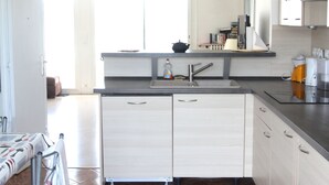 Une cuisine moderne avec des meubles blancs, un plan de travail en acier inoxydable et un sol carrelé.