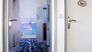 Un couloir étroit, dont le sol est pavé de pierres, mène à une porte sur laquelle est affiché un panneau indiquant « Toilettes ».
