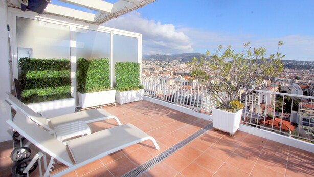 Un balcon avec des chaises blanches, un pot de fleurs et une vue sur le paysage urbain.