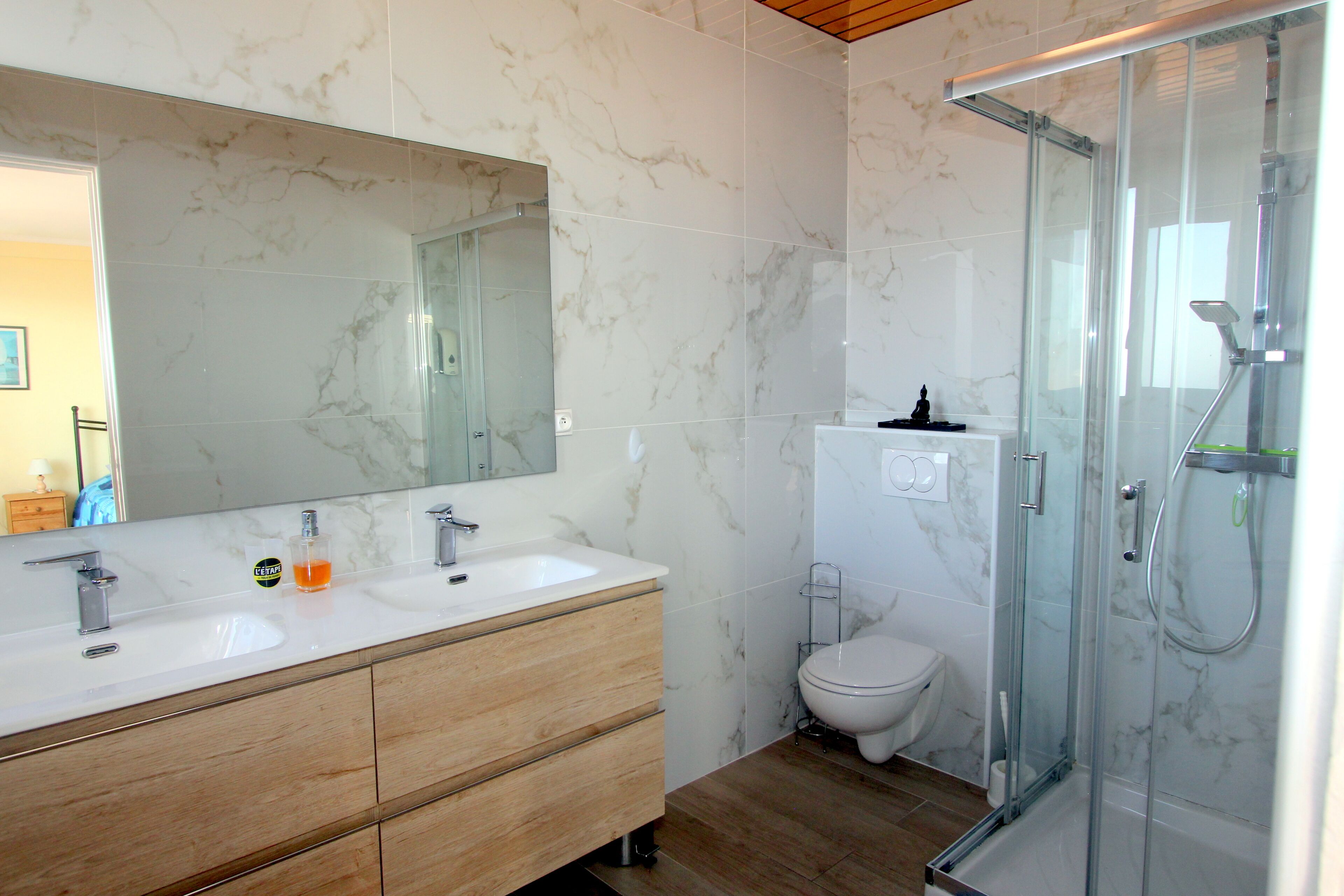 Een moderne badkamer met marmeren wanden, een houten wastafelmeubel, een glazen douchecabine en een toilet.