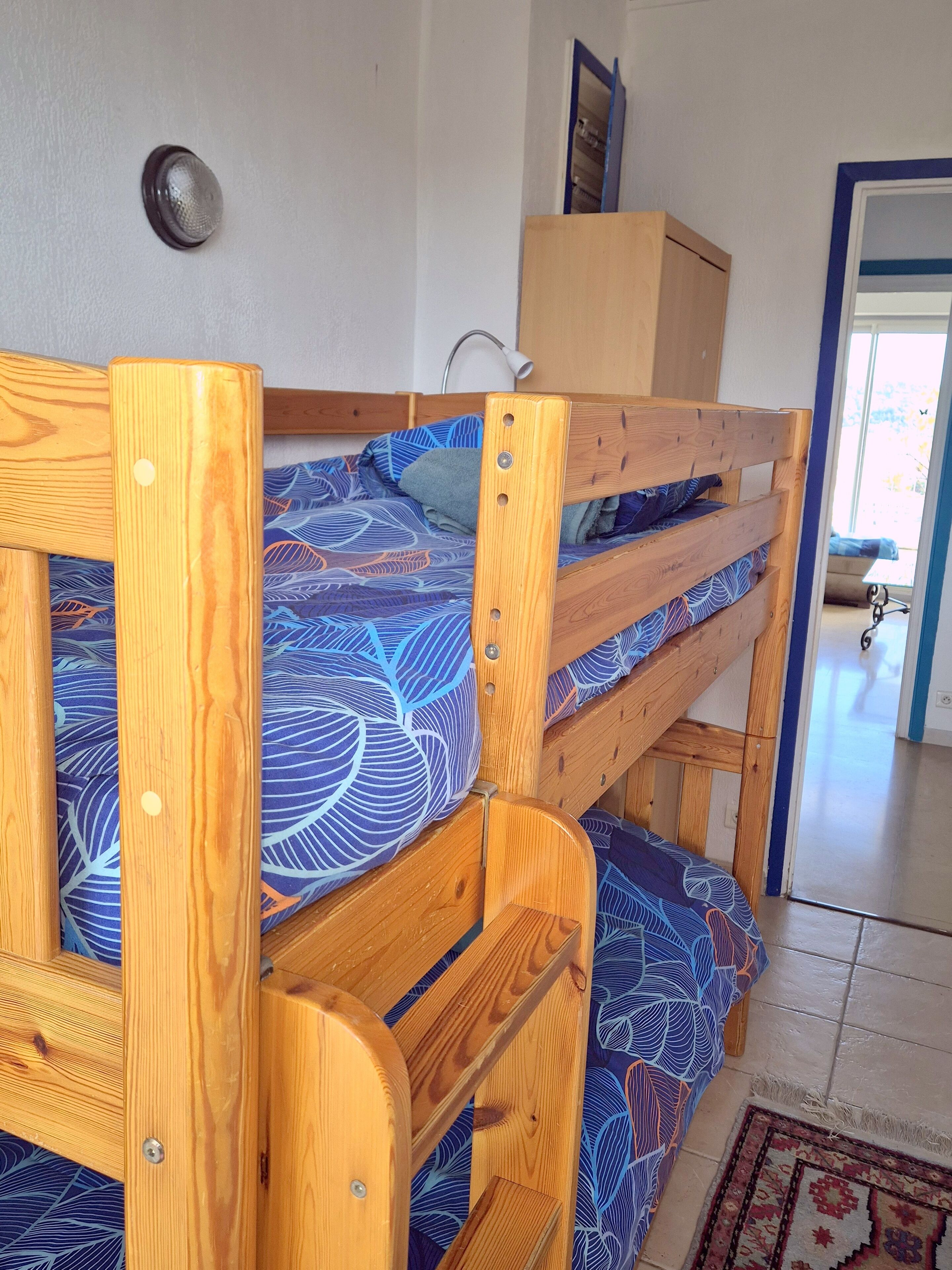 Un lit superposé avec une couvre-lit à motifs, une tête de lit en bois et un petit placard au-dessus.