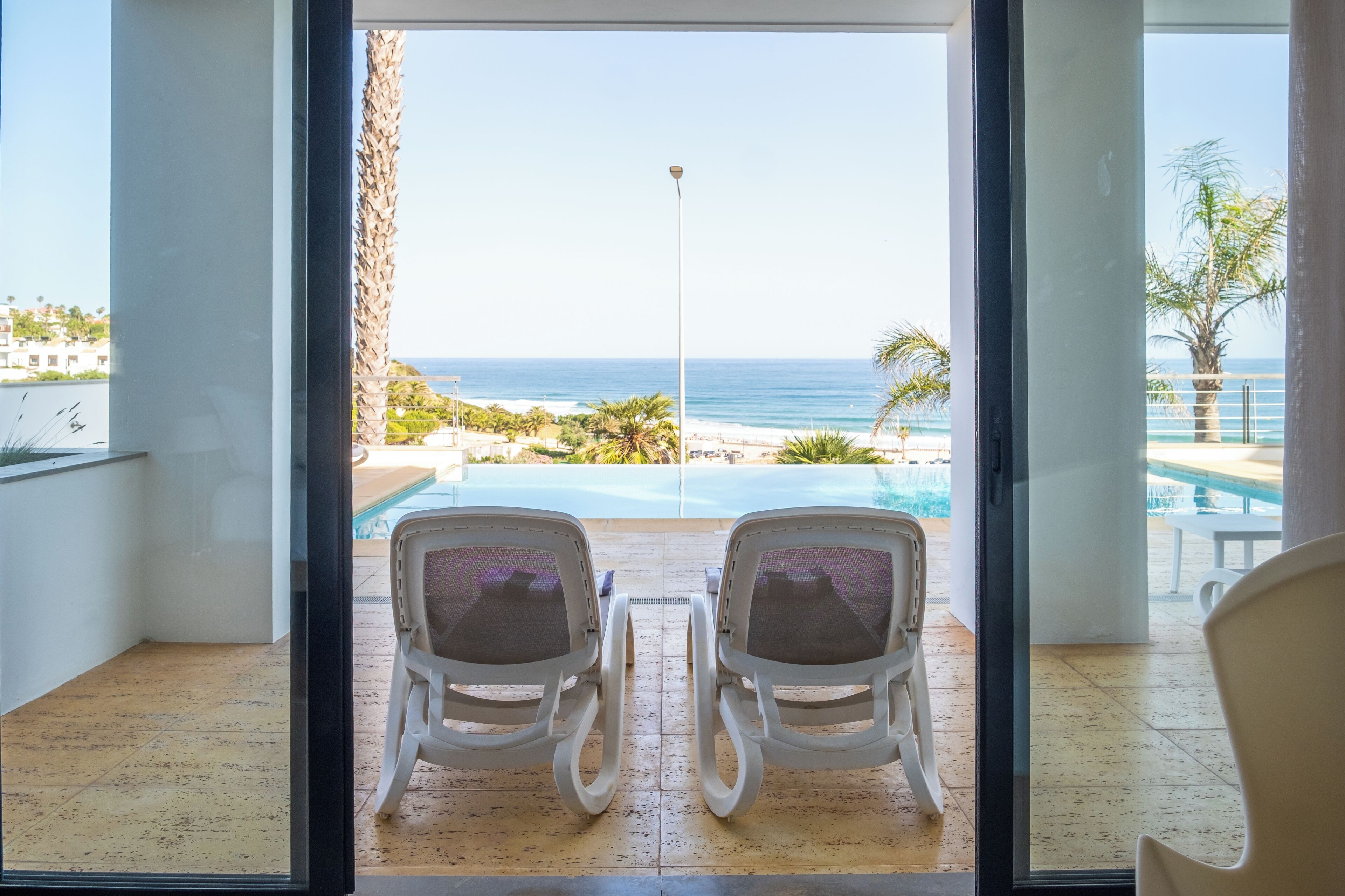A room with two chairs facing a pool and a view of the ocean.