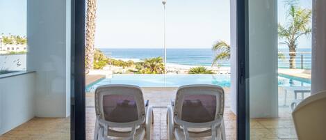 A room with two chairs facing a pool and a view of the ocean.