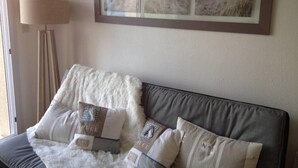 Un dormitorio con un sofá gris, un plaid blanco y esponjoso, y un cuadro con dunas de arena.