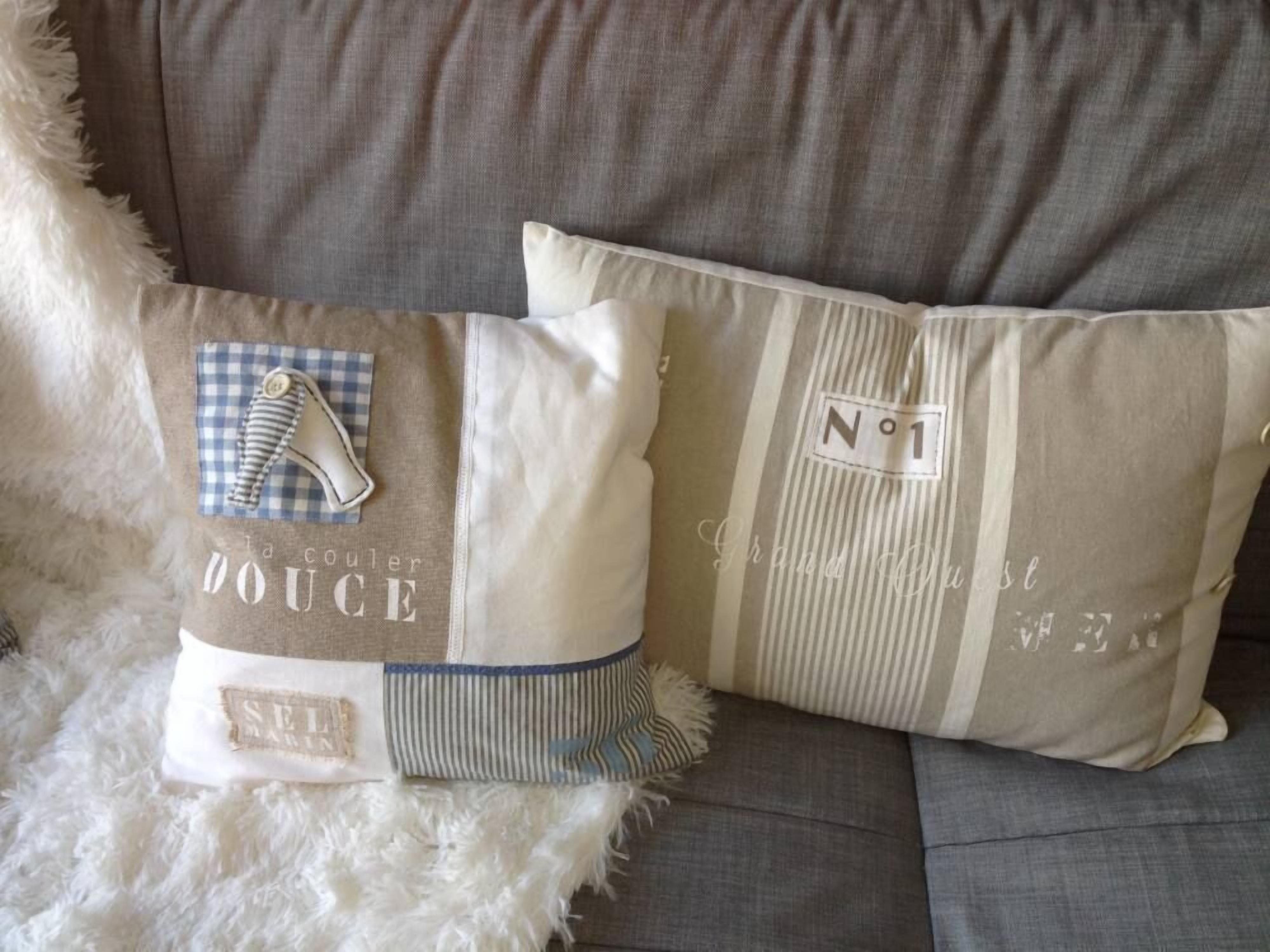 Un sofá gris con dos almohadones decorativos, uno con estampado de cuadros y el otro con rayas, ambos con texto y un botón.