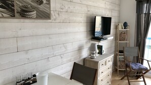 Una habitación con pared de madera, un televisor sobre una estantería, un escritorio con lámpara y una silla.