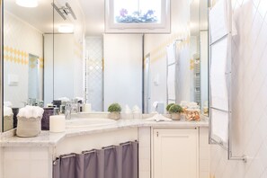 Ein modernes Badezimmer mit großem Spiegel, zwei Waschbecken, einer Dusche und einem Waschtisch mit Pflegeprodukten.