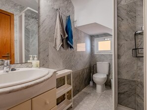 Et badeværelse med en marmorvæg, en vask, et toilet og et bruseområde.