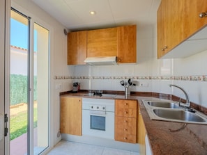 A compact kitchen with wooden cabinets, a built-in oven, a stovetop, and a sink.