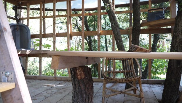 A wooden deck with a table and a wicker chair, surrounded by a wooden fence and trees. - Beautiful house with big garden and private pool (Mazan)