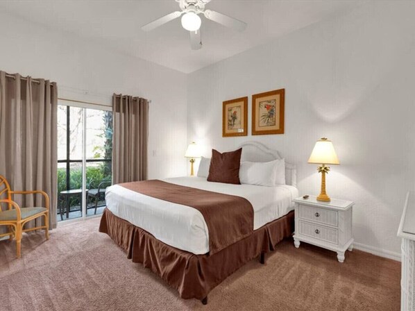 A hotel room with a large bed, two bedside tables with lamps, a chair, and a balcony with curtains. - 3 Bedroom Apartment near Disney World (Davenport)