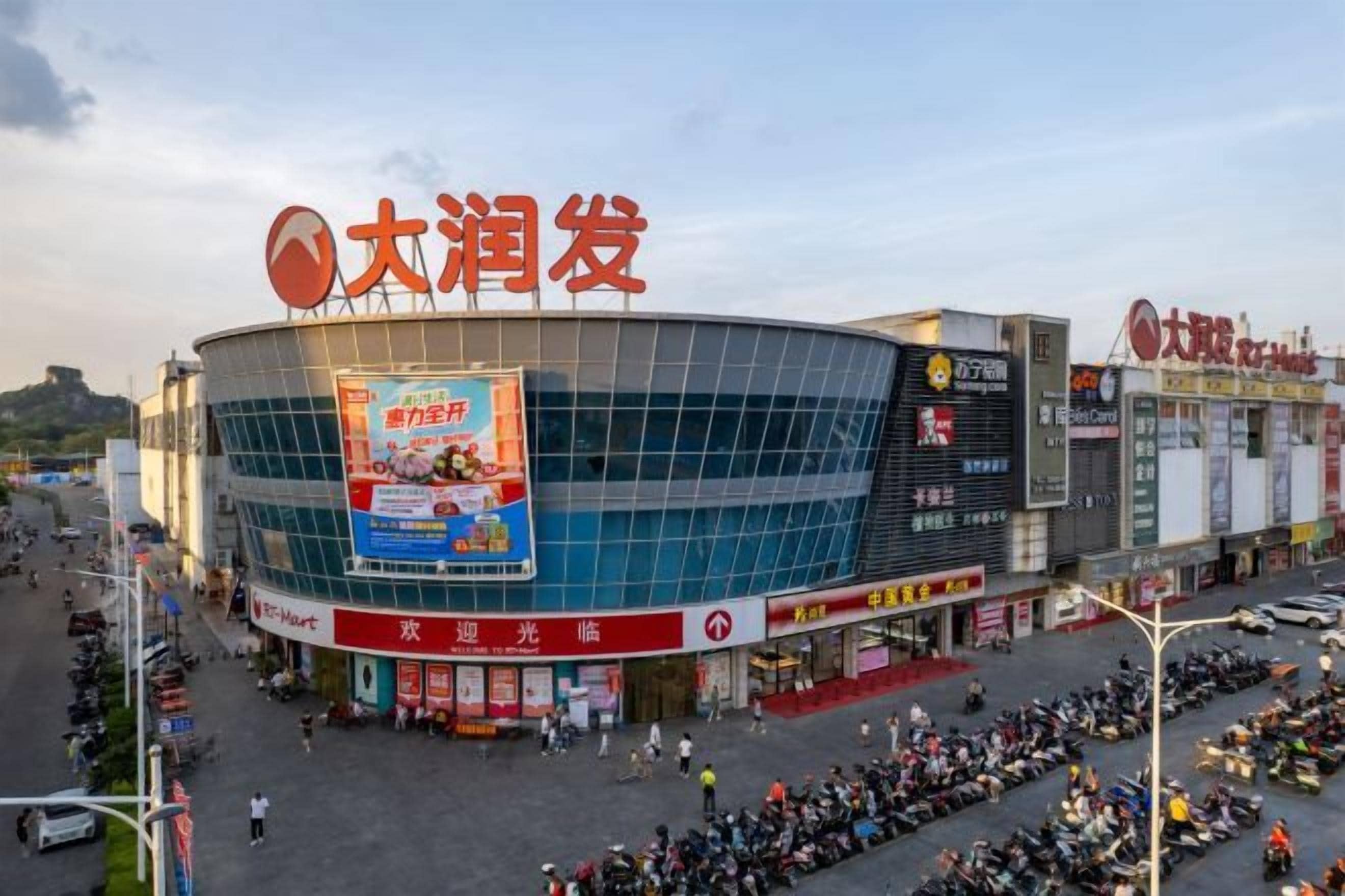 A large stadium with a prominent sign, surrounded by commercial buildings and a busy street with parked motorcycles.