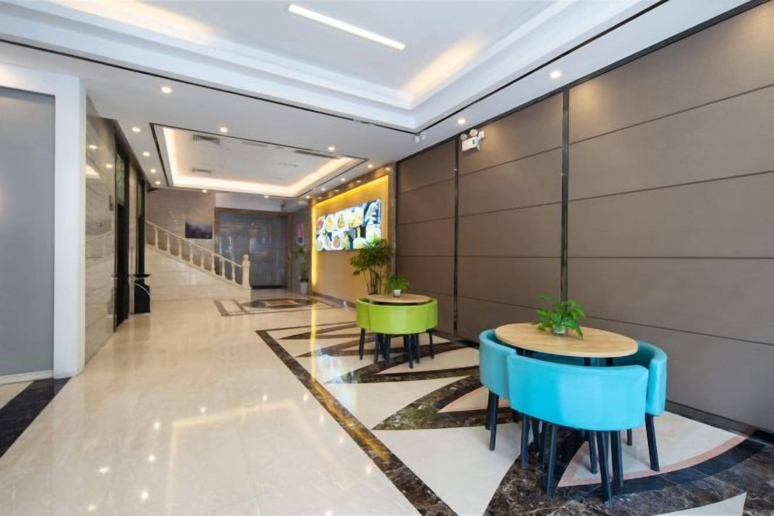 Vestíbulo de hotel con mostrador de recepción, una escalera y un área de descanso con mesas redondas.