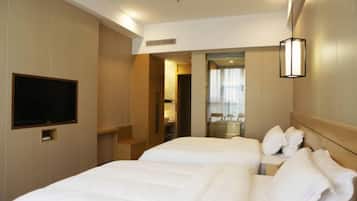 Een hotelkamer met twee bedden, een flatscreen televisie aan de muur, een spiegel en een raam met gordijnen.