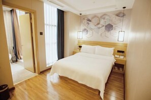 A hotel room with a wooden floor, a bed with white bedding, a nightstand with a lamp, and a wall with hexagonal patterns. - Huifeng Xiangxing Hotel (Liuzhou)