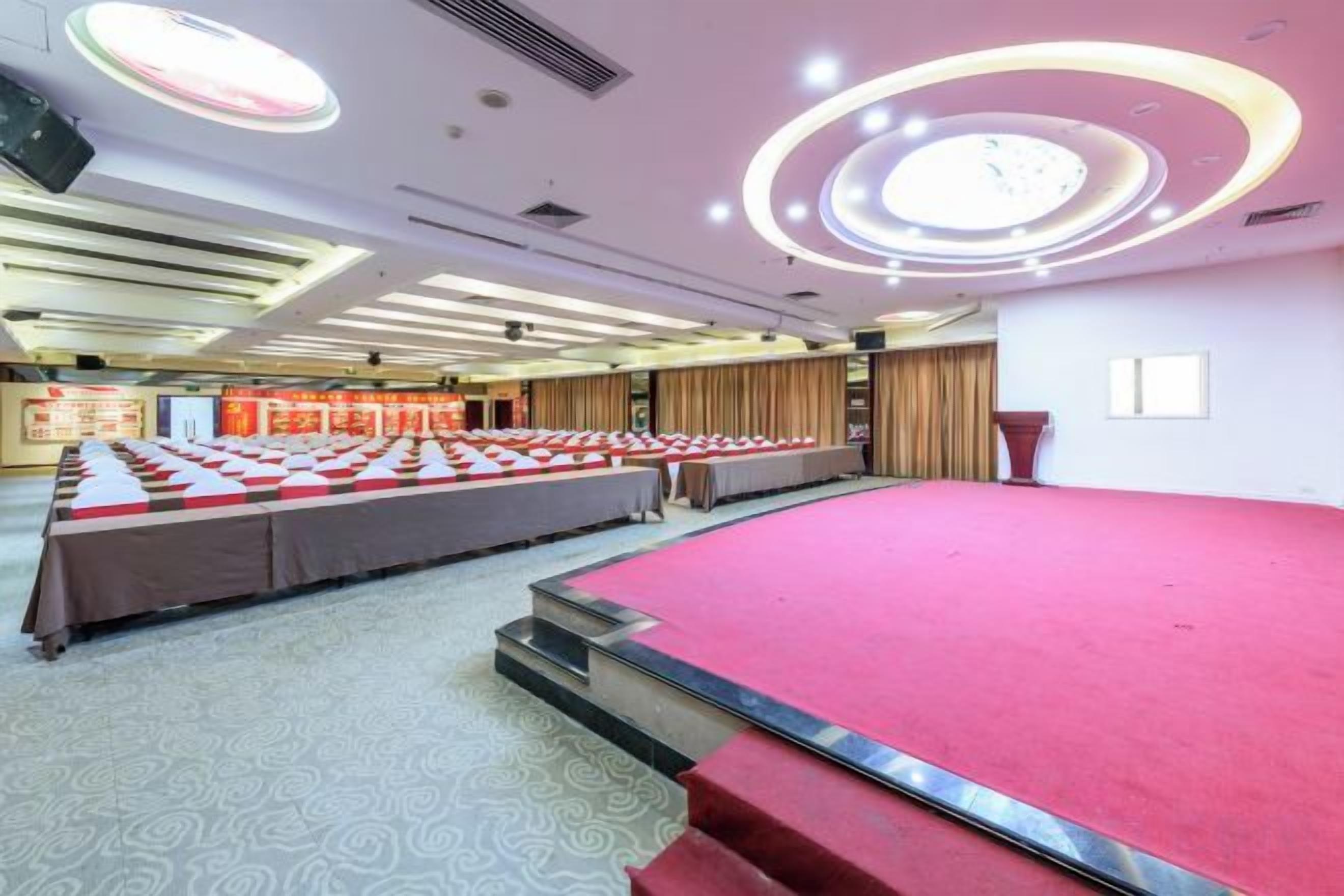 A conference room with a stage, long tables, and a carpeted floor.