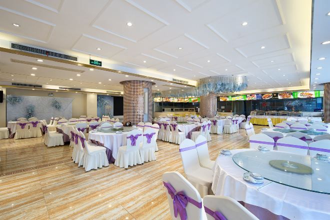 A banquet hall with round tables and chairs, a central pillar, and a dining area with a counter.