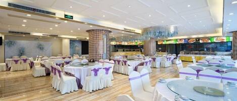 Un salón de banquetes con mesas y sillas redondas, un pilar central y una zona de comedor con mostrador.