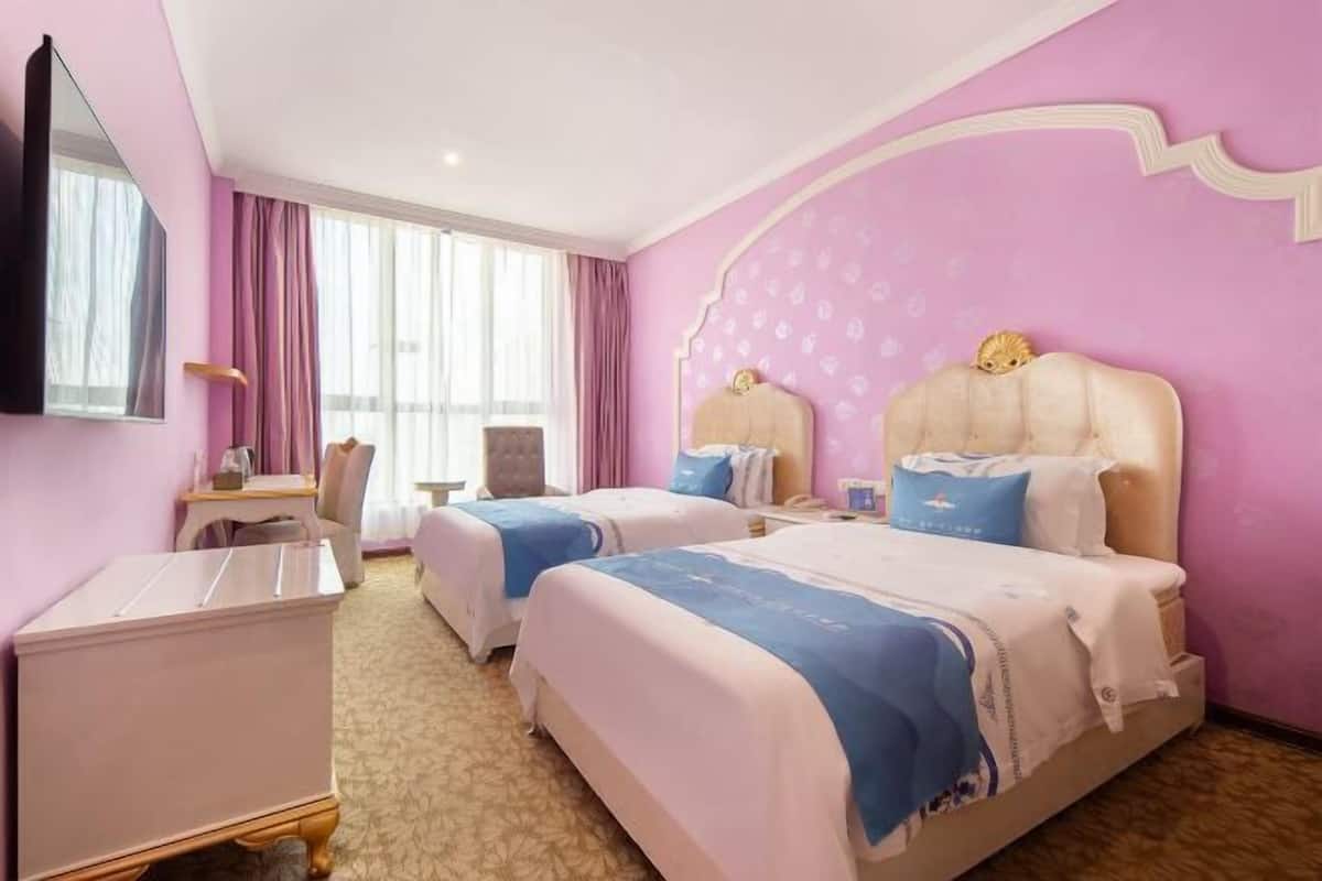 A hotel room with two beds, a desk, a chair, and a television.