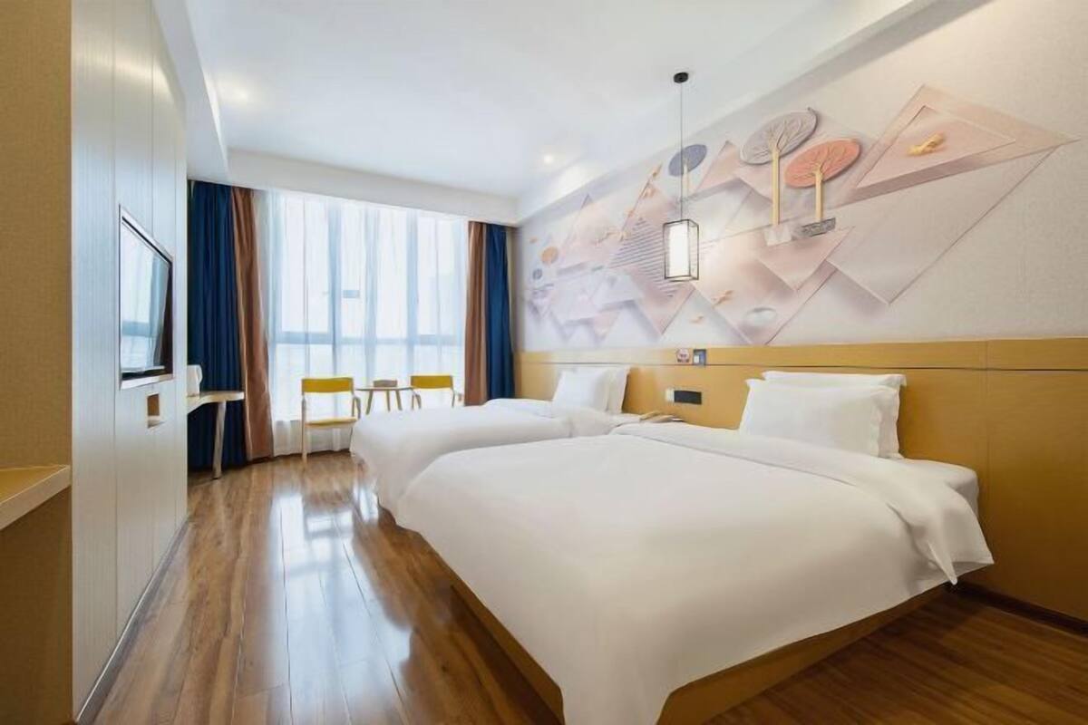 A hotel room with two beds, a TV, a desk, and a window with curtains.