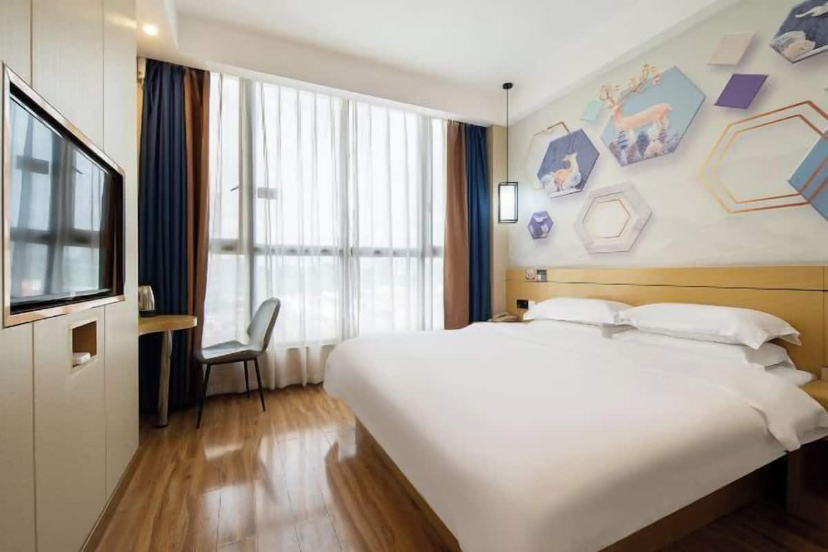 A hotel room with a bed, a desk, a chair, a TV, and a large window with curtains.