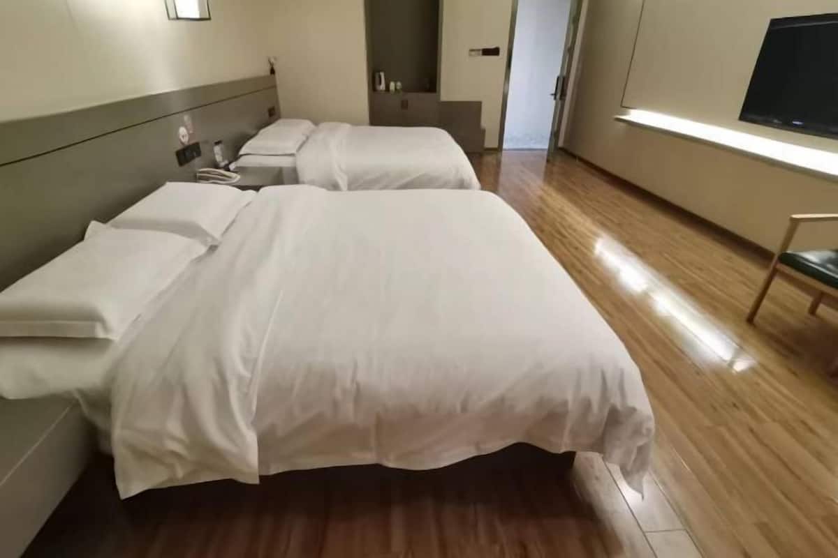 A hotel room with two beds, a TV, and a wooden floor.