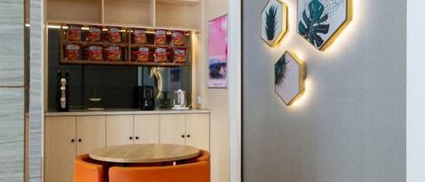 Una cocina moderna con cafetera integrada, un área de descanso con sillas naranjas y decoración en la pared.